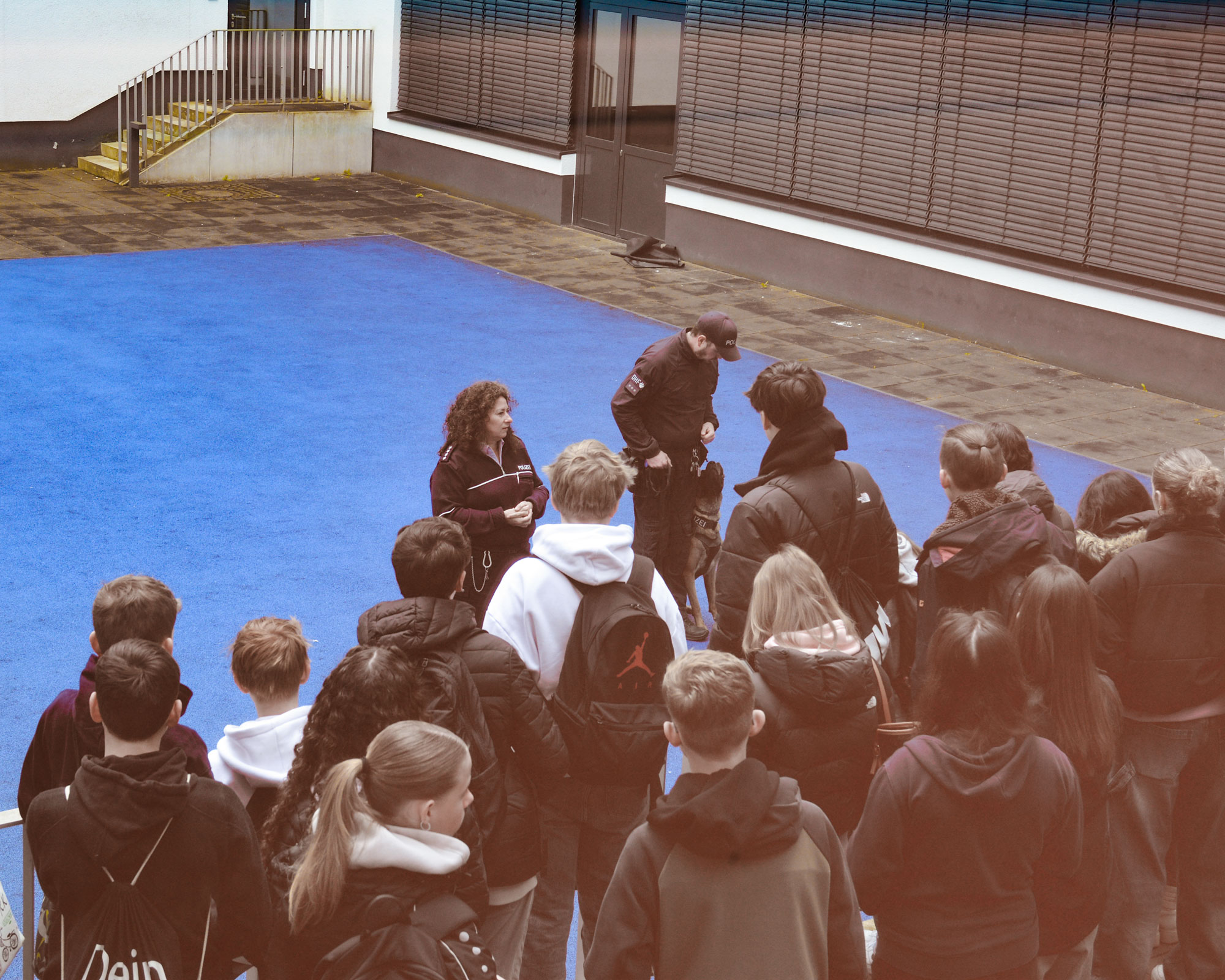 Schülerinnen und Schüler hören dem Vortrag der Diensthundestaffel zu und sehen einen trainierenden Diensthund
