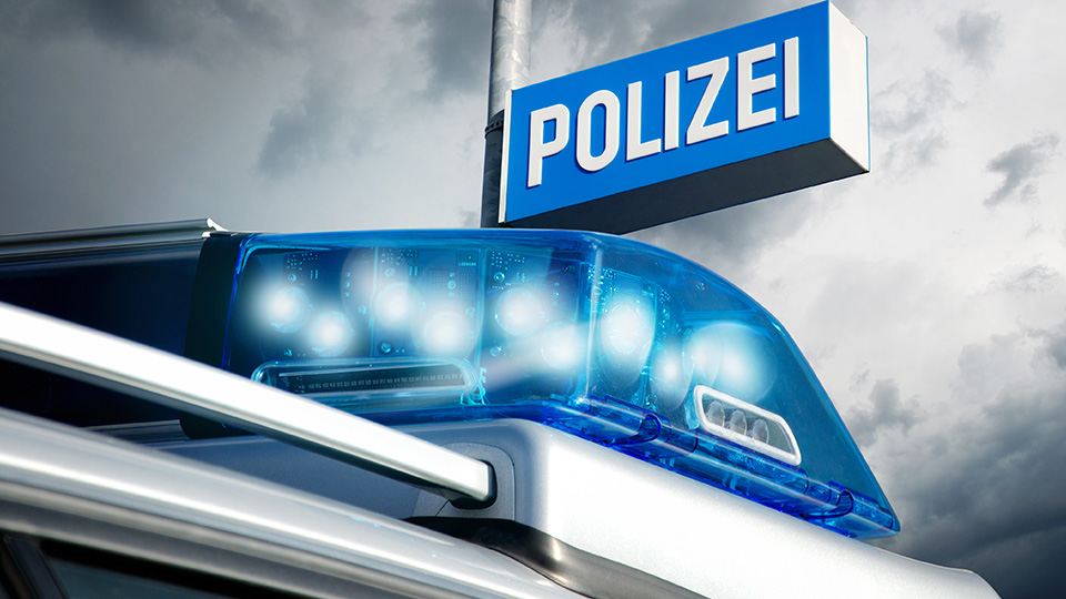 Man sieht ein Blaulicht eines Streifenwagens sowie ein Polizeischild in blau. 