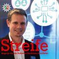 Alexander Prim, Leiter des Projektes Digitale Verwaltung der Polizei NRW und Ulrike Nehnes von der Pilotbehörde Wesel stehen vor einem großen Bildschirm, auf dem eine Grafik des DVPol Projektes zu sehen ist. Im Vordergrund ist in rot der Schriftzug "Streife, das Magazin für die Polizei Nordrhein-Westfahlen zu sehen.