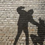 Mauer mit Schatten von zwei Personen, eine Person hebt Faust in Richtung sitzender Person