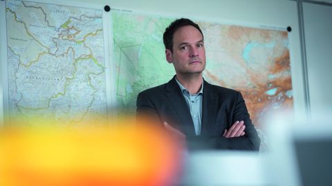 Jochen Bäcker from the LKA NRW stands in an office with his hands clasped. Large maps can be seen on a wall in the background.