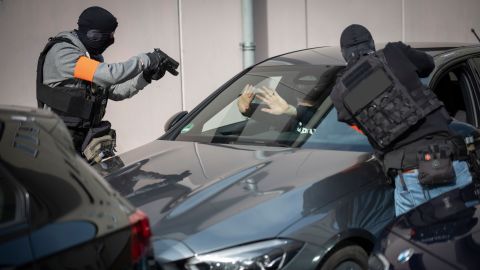 Two officers from the mobile task force stop a car during an exercise. They point guns at the driver. The driver holds his hands out in defense.