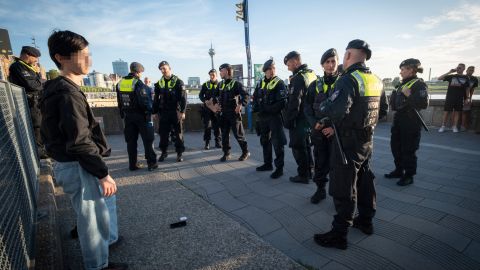 Polizistinnen und Polizisten umstellen einen 14 jährigen Jungen , bevor sie ihn zur Wache bringen. Im Hintergrund ist der Rhein zu sehen.