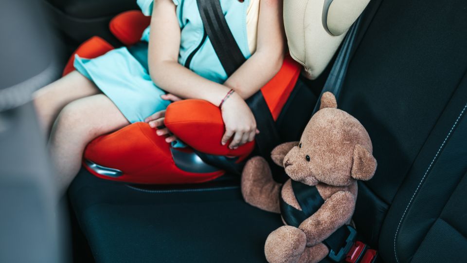 Kleinkind, angeschnallt im Kindersitz im Auto. Daneben ein Teddy, ebenfalls angeschnallt.