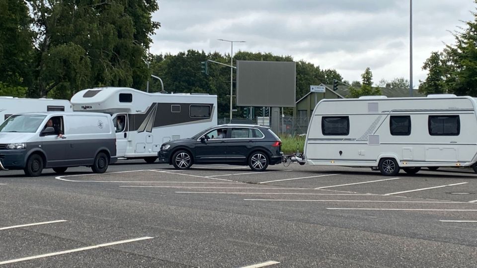 Auf einem Parkplatz hat sich eine Schlange aus wartenden Wohnmobilen und Wohnwagen gebildet. 