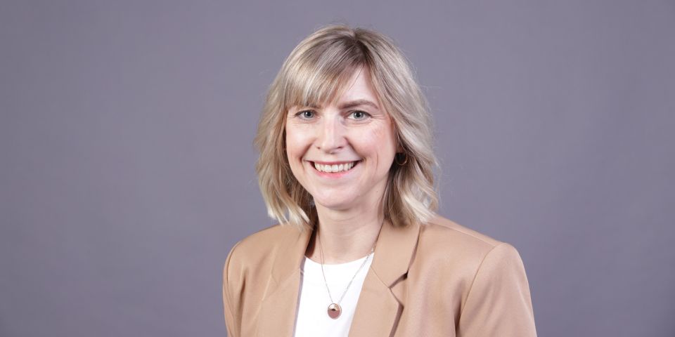 Blonde Mitarbeiterin der Pressestelle in einem weißen T-Shirt und beigem Blazer